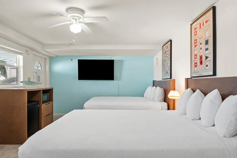Chambre lumineuse avec deux lits et un téléviseur mural.