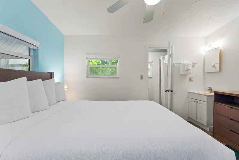 Chambre lumineuse avec un grand lit recouvert de blanc et un coin lavabo.