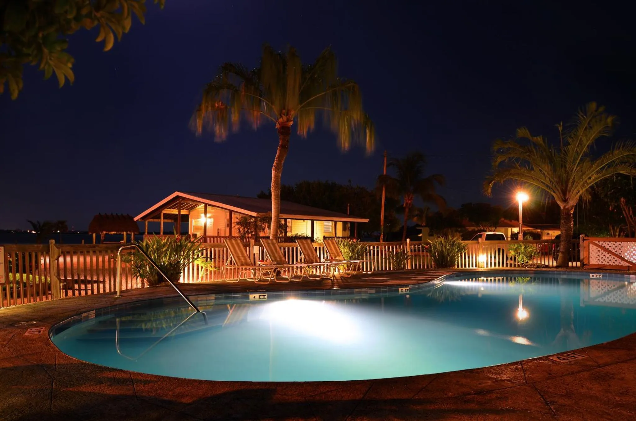 Une piscine illuminée au crépuscule, entourée de végétation tropicale et de chaises longues.