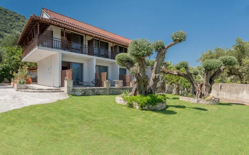 Bâtiment blanc à deux étages avec des balcons et un jardin verdoyant.