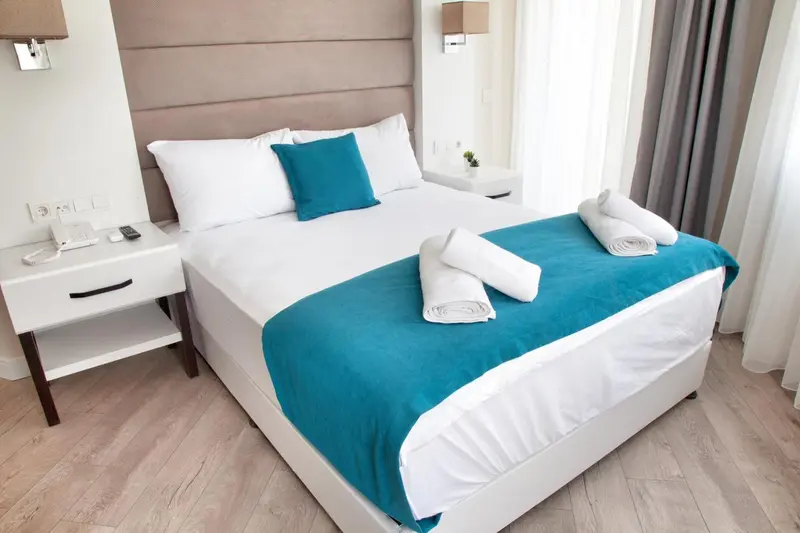 Une chambre lumineuse avec un grand lit recouvert d'une courtepointe turquoise et de coussins.