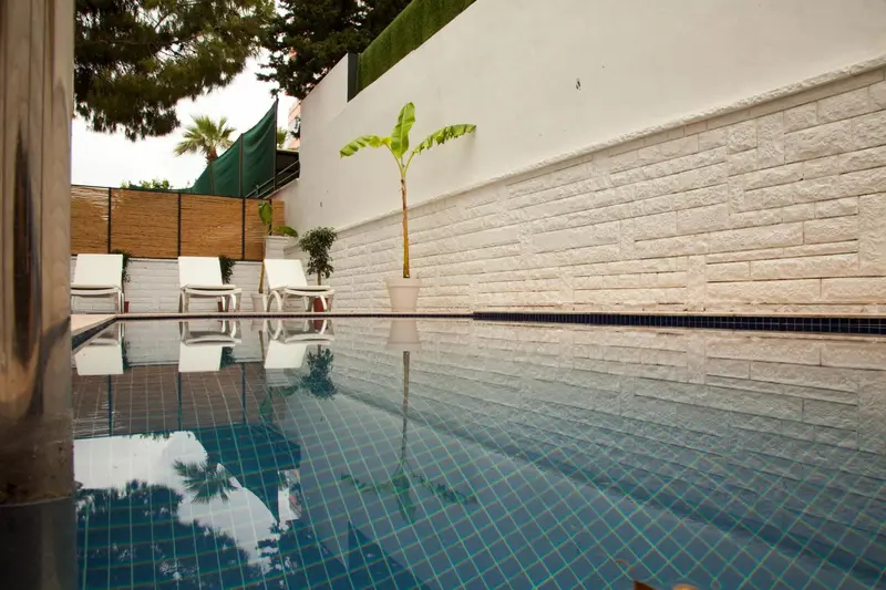 Petite piscine rectangulaire avec transats blancs et végétation luxuriante.