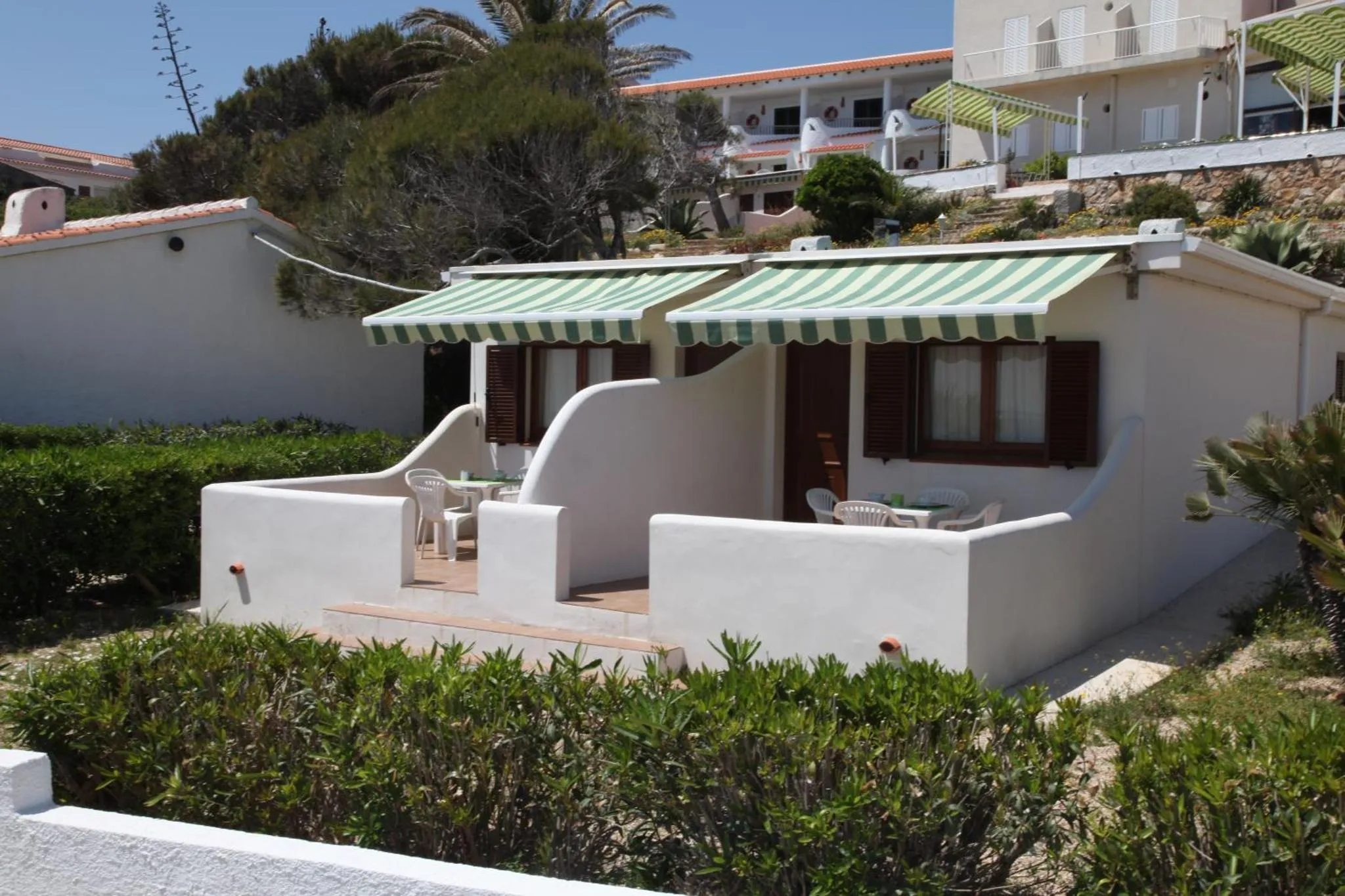 Petite maison blanche avec une terrasse ombragée et une végétation luxuriante.