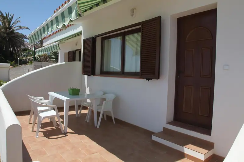 Une terrasse avec une table et des chaises devant une porte marron.