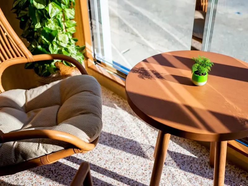 Un fauteuil en rotin et une table ronde éclairées par le soleil.