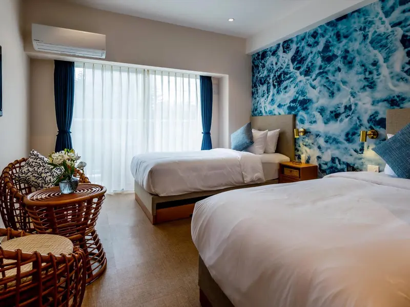Chambre lumineuse avec deux lits simples et un coin salon.