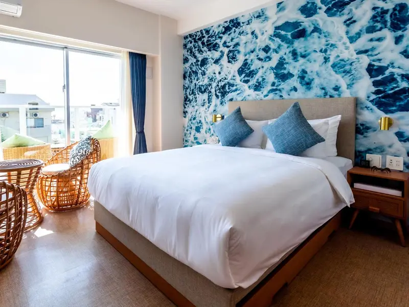 Chambre lumineuse avec un grand lit et un mur décoratif évoquant les vagues.