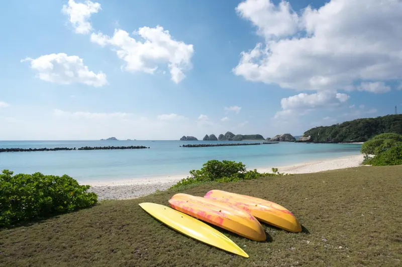Deux kayaks reposent sur une pelouse verdoyante face à une plage de sable blanc et une mer turquoise.