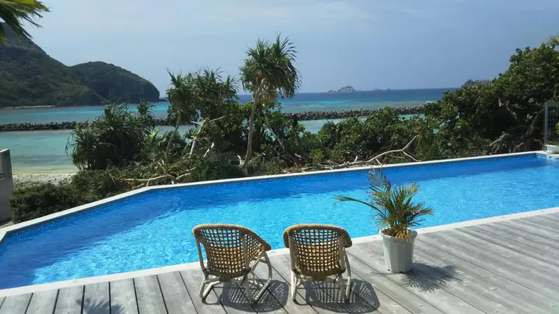 Deux fauteuils en osier sont placés au bord d'une piscine turquoise avec vue sur la mer.