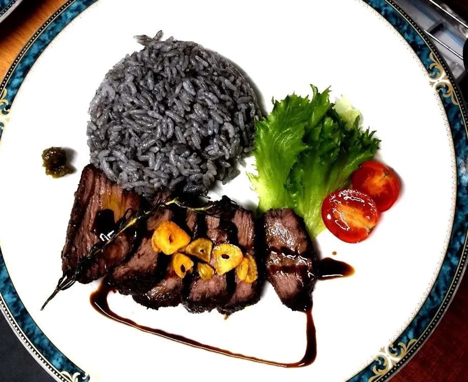 Assiette de viande grillée accompagnée de riz noir et de légumes frais.