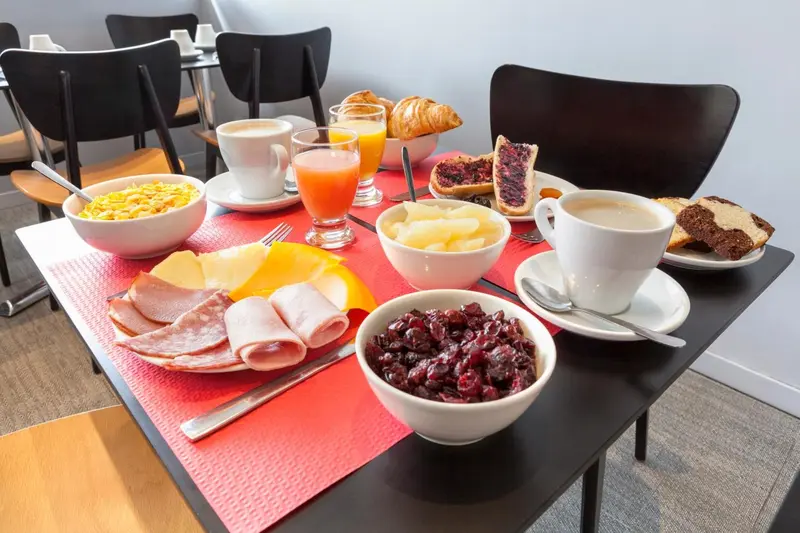 Une table est dressée pour le petit-déjeuner avec des viennoiseries, des fruits et des boissons.