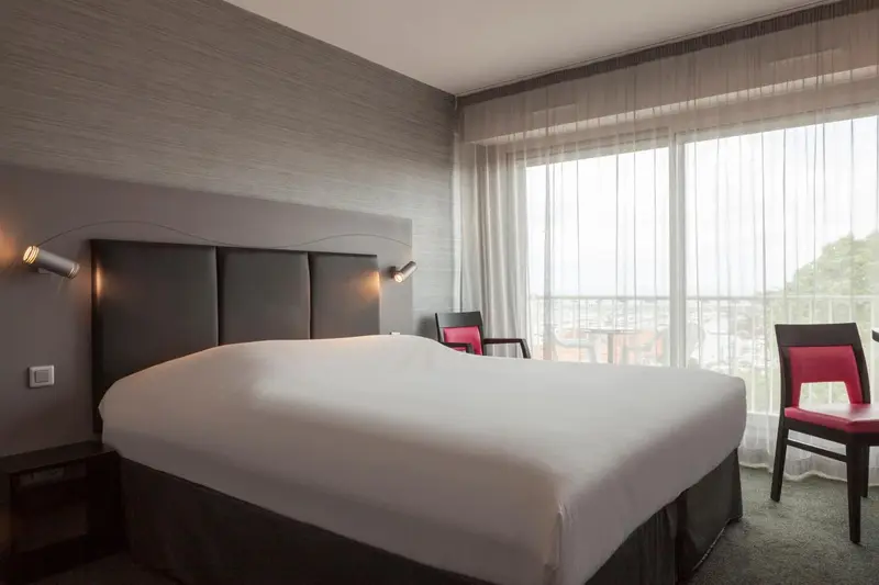Une chambre d'hôtel lumineuse avec un grand lit et un fauteuil près de la fenêtre.