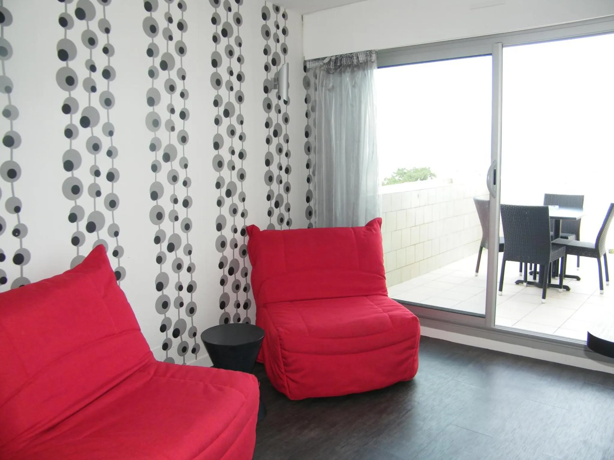 Espace de détente intérieur avec canapés rouges et accès à une terrasse.