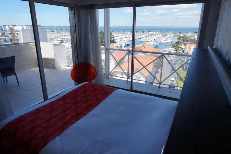 Une chambre avec un lit donnant sur une vue mer et un port de plaisance.