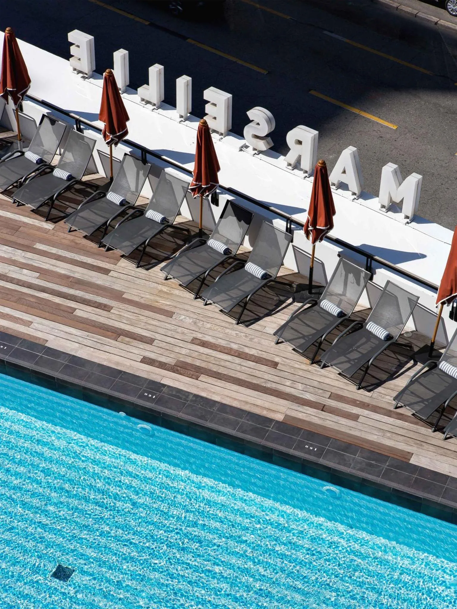 Transats alignés au bord d'une piscine turquoise sous le soleil.