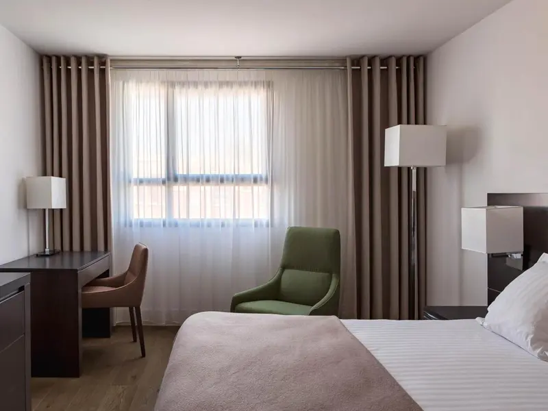 Une chambre lumineuse avec un lit, un bureau et un fauteuil.
