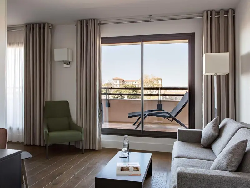 Espace de séjour lumineux avec canapé, fauteuil et accès à une terrasse.