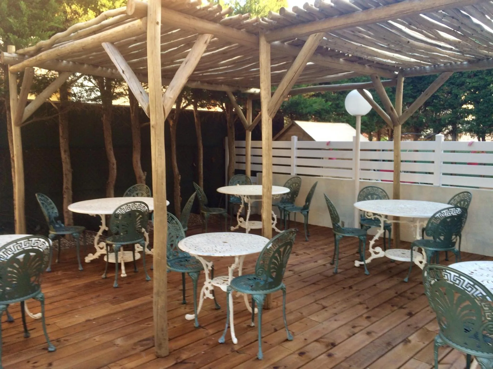 Terrasse ombragée avec tables et chaises en fer forgé.