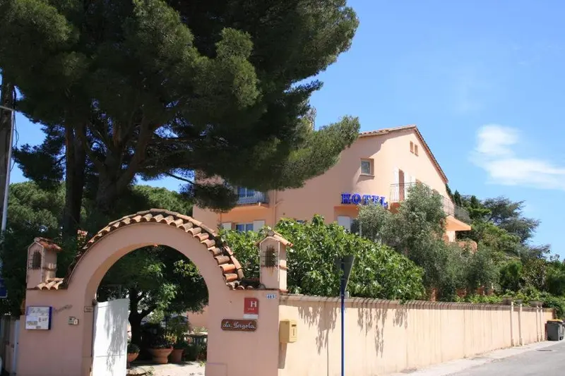 Façade d'un bâtiment rose avec une entrée arquée et une végétation luxuriante.