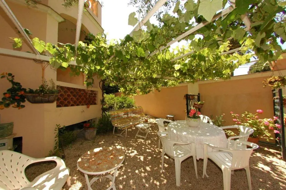 Une table et des chaises blanches sont disposées sur une terrasse ombragée par de la végétation.