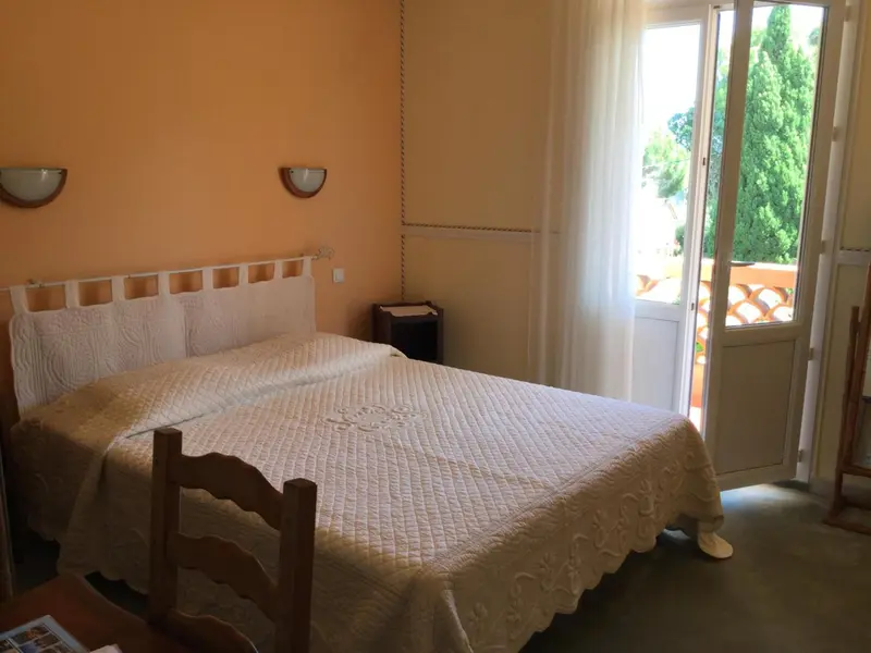 Une chambre lumineuse avec un lit recouvert d'une courtepointe blanche et une porte-fenêtre donnant sur l'extérieur.