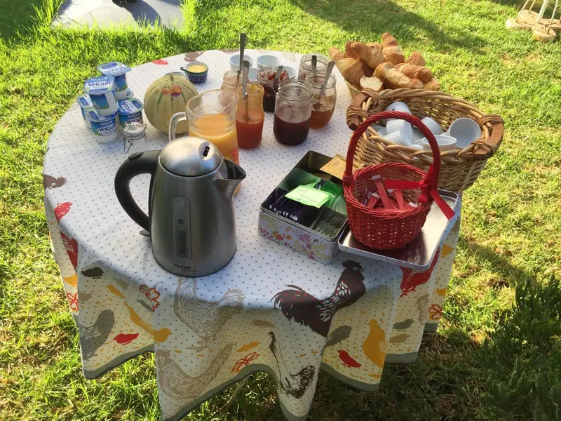 Une table ronde est dressée avec des viennoiseries, des fruits, des yaourts et des boissons.