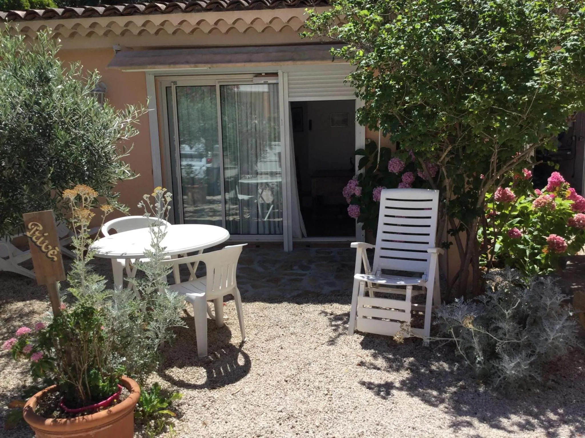 Une table et des chaises blanches sont disposées devant une terrasse ombragée.