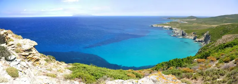 Vue panoramique sur une crique turquoise bordée de végétation et de rochers.