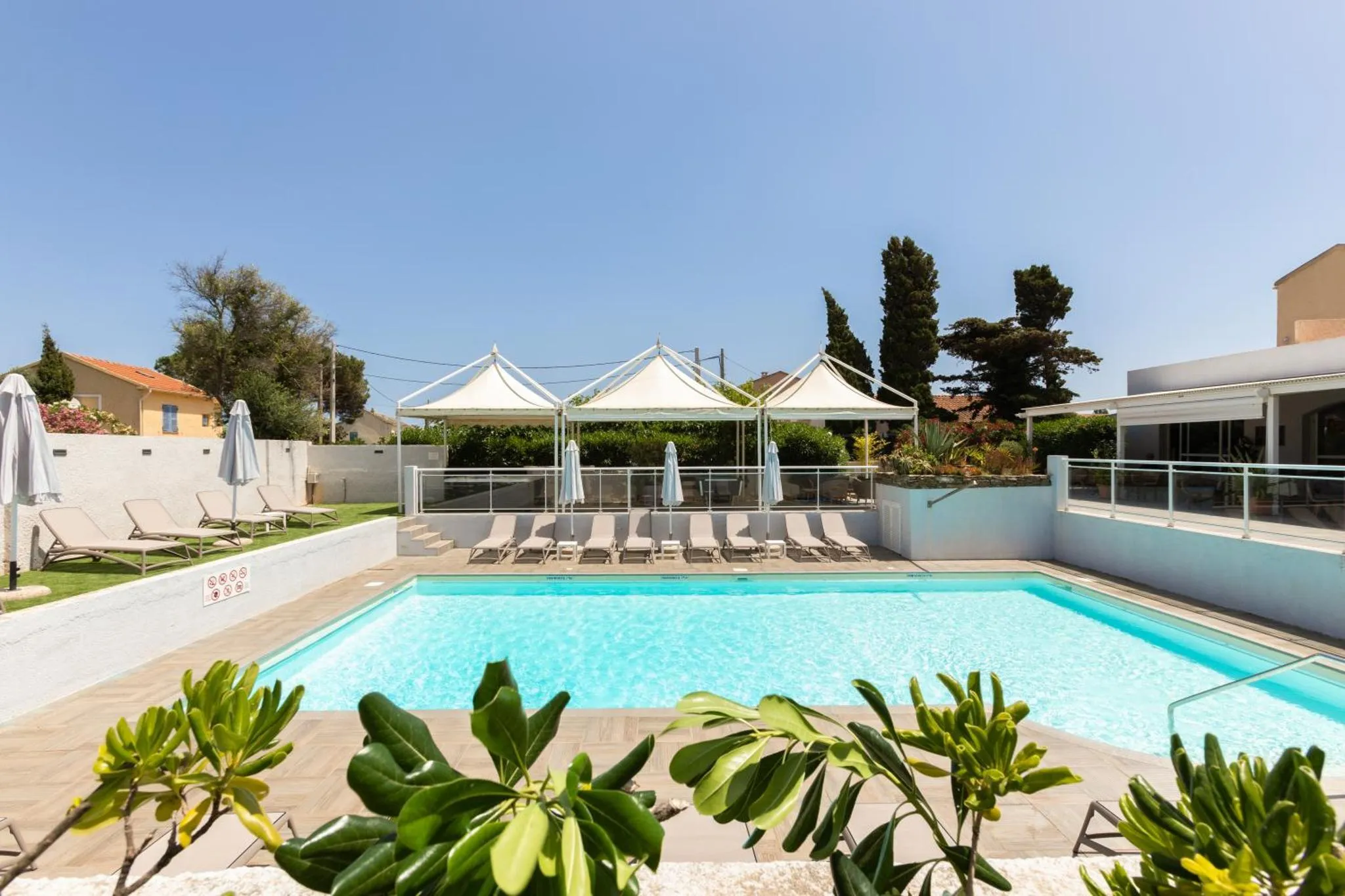 Piscine rectangulaire entourée de chaises longues et d'une terrasse ombragée.