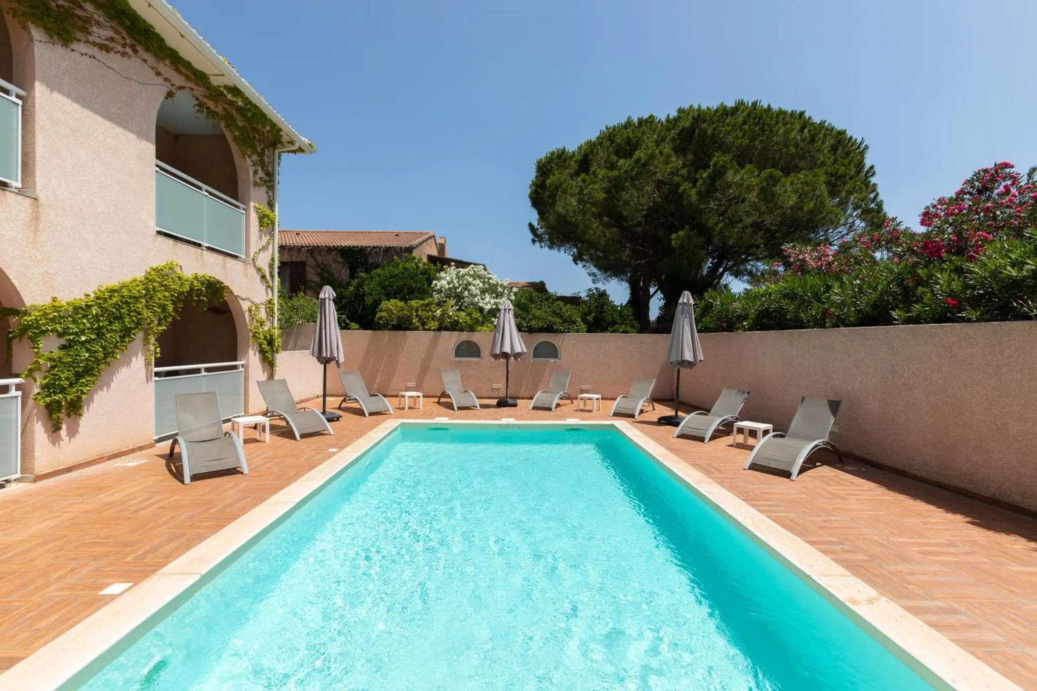 Une piscine rectangulaire bordée d'une terrasse avec des transats et des parasols.