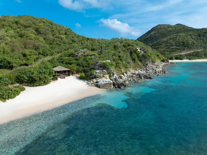 Vue aérienne d'une plage de sable blanc bordée d'une eau turquoise et d'une végétation luxuriante.
