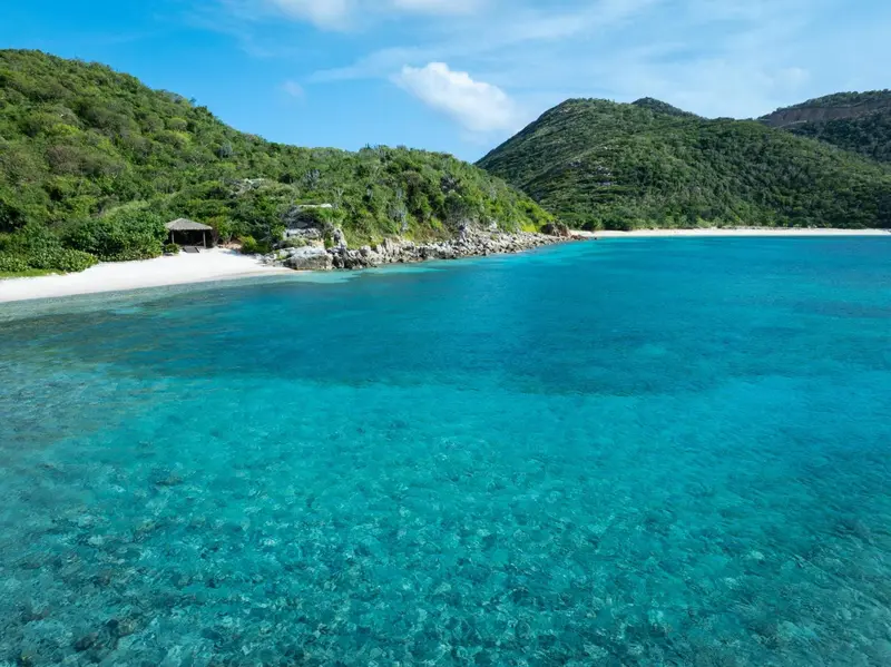 Vue aérienne d'une plage de sable blanc bordée d'une eau turquoise et d'une végétation luxuriante.
