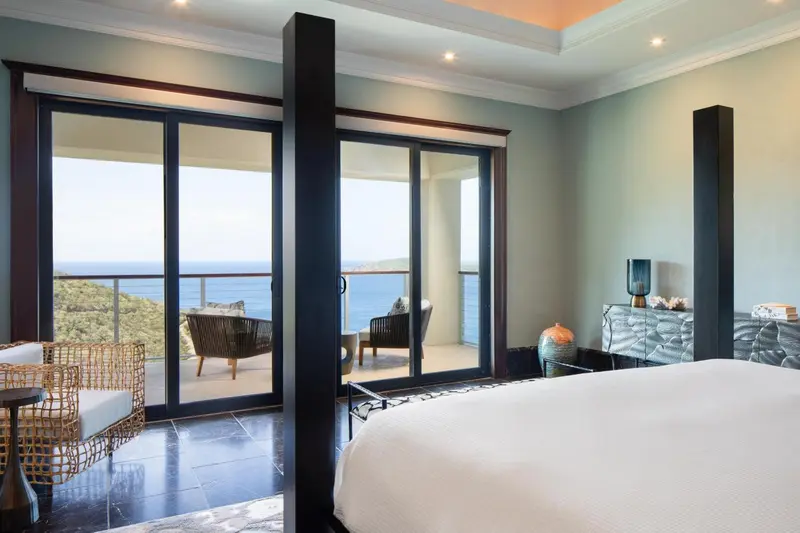 Chambre lumineuse avec un grand lit et une vue sur la mer depuis une terrasse.