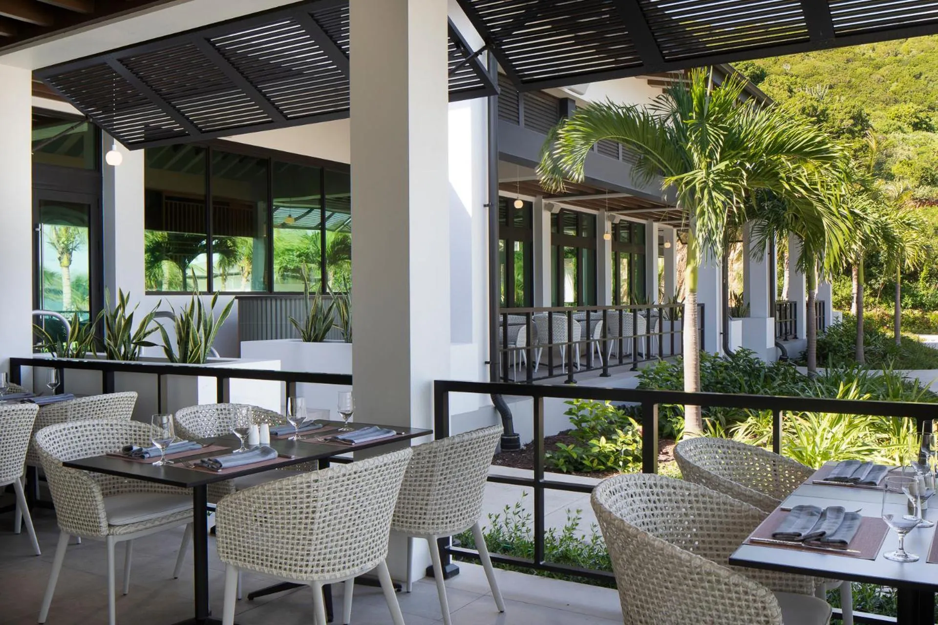 Tables dressées en terrasse ombragée avec une végétation luxuriante en arrière-plan.