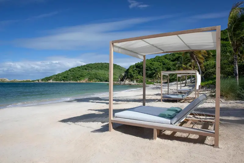 Transats sous des pergolas sur une plage de sable blanc.