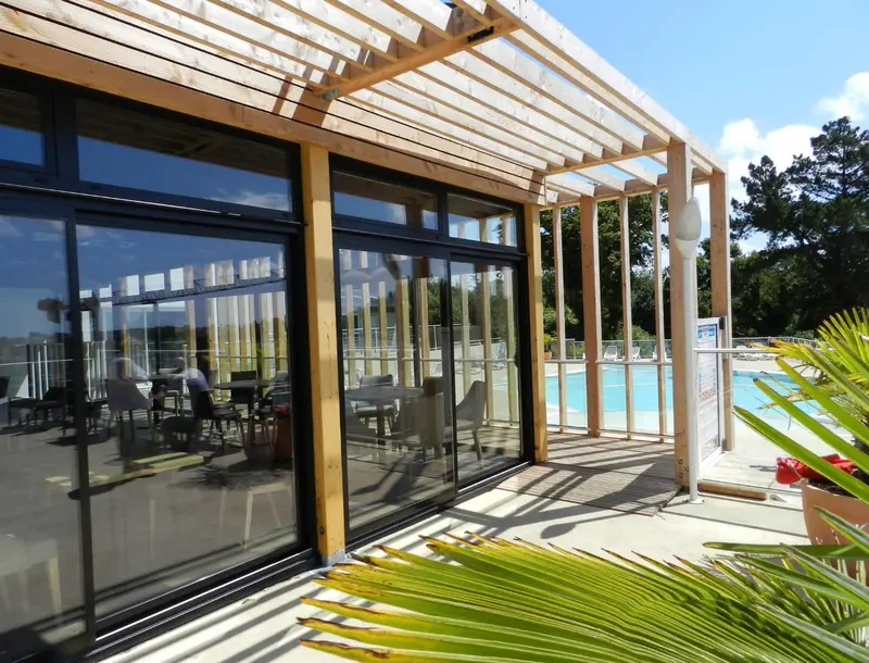 Terrasse ombragée donnant sur une piscine ensoleillée.