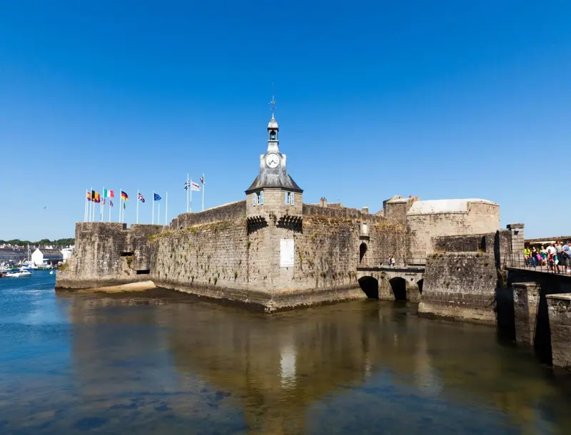 Forteresse historique en pierre bordant un port ensoleillé.