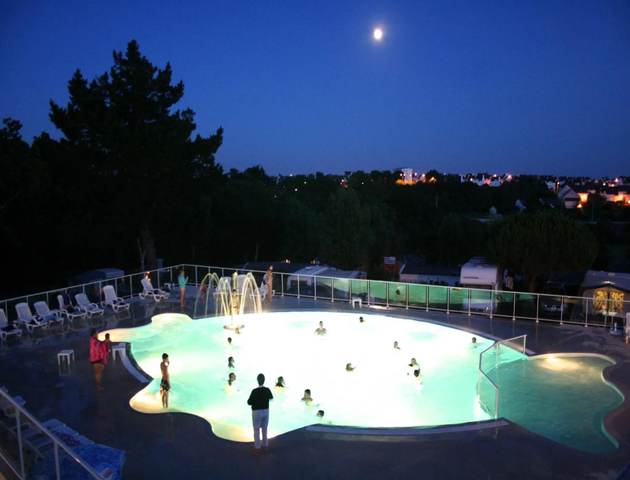 Une piscine illuminée au crépuscule avec des personnes se baignant.