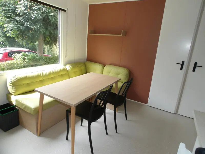 Un coin repas lumineux avec une banquette verte et une table en bois.