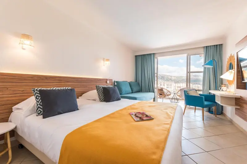 Chambre lumineuse avec un grand lit et un coin salon donnant sur une vue dégagée.