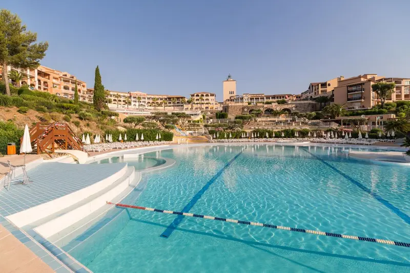 Une piscine bleue avec des transats et des parasols, devant un complexe hôtelier.