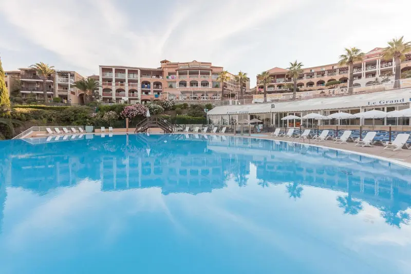 Vue d'une piscine turquoise reflétant un bâtiment blanc et des palmiers sous un ciel bleu.