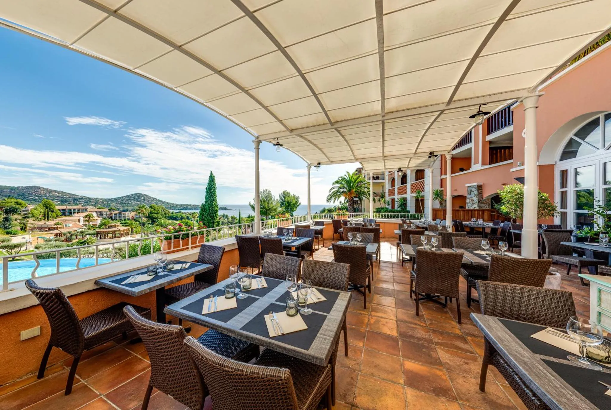Terrasse ombragée avec tables et chaises donnant sur la mer.