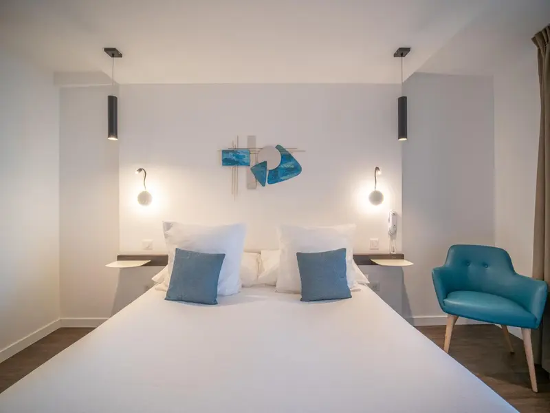 Une chambre lumineuse avec un grand lit et un fauteuil turquoise.