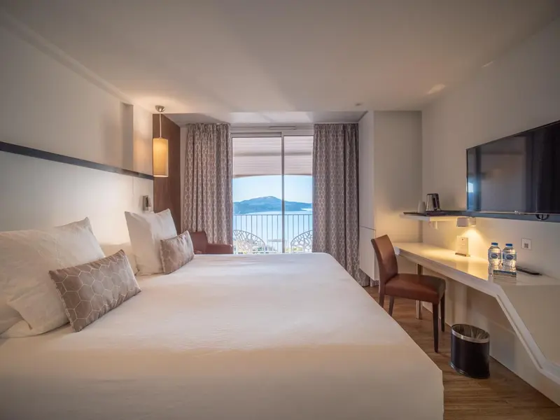 Chambre lumineuse avec un grand lit et vue sur la mer.
