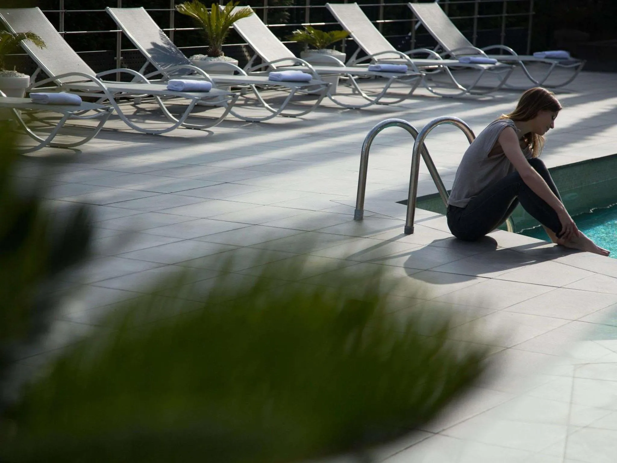 Une femme est assise au bord d'une piscine ensoleillée.