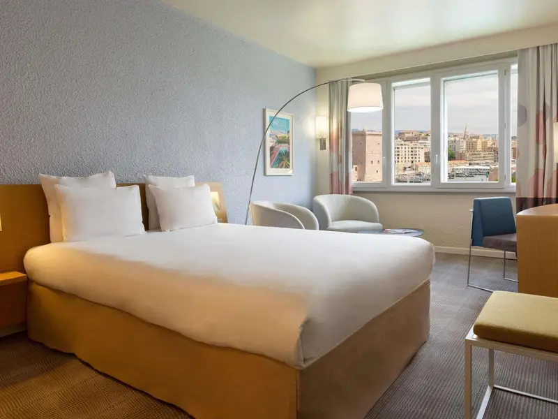 Une chambre lumineuse avec un grand lit et une vue sur la ville.