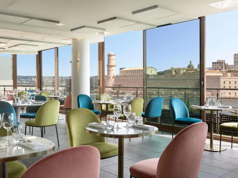 Une salle de restaurant lumineuse offre une vue sur la ville et le port.