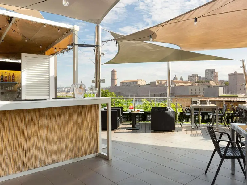 Terrasse ombragée avec un bar et des tables donnant sur une ville côtière.