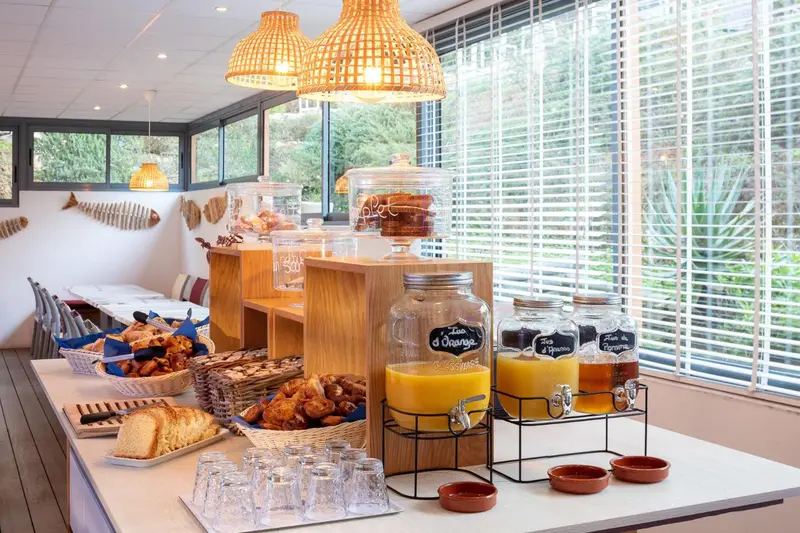 Un buffet propose des viennoiseries, des jus de fruits et des céréales dans une salle lumineuse.